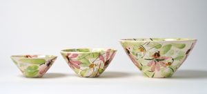 A photo of three ceramic bowls arranged in a row. The smallest is on the left while the largest is on the right. All three feature a hand painted floral design.