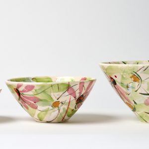 A photo of three ceramic bowls arranged in a row. The smallest is on the left while the largest is on the right. All three feature a hand painted floral design.
