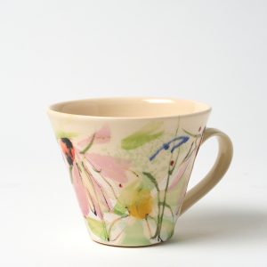 A photo of a hand thrown ceramic cup. It has a hand painted floral design on a light background glaze.