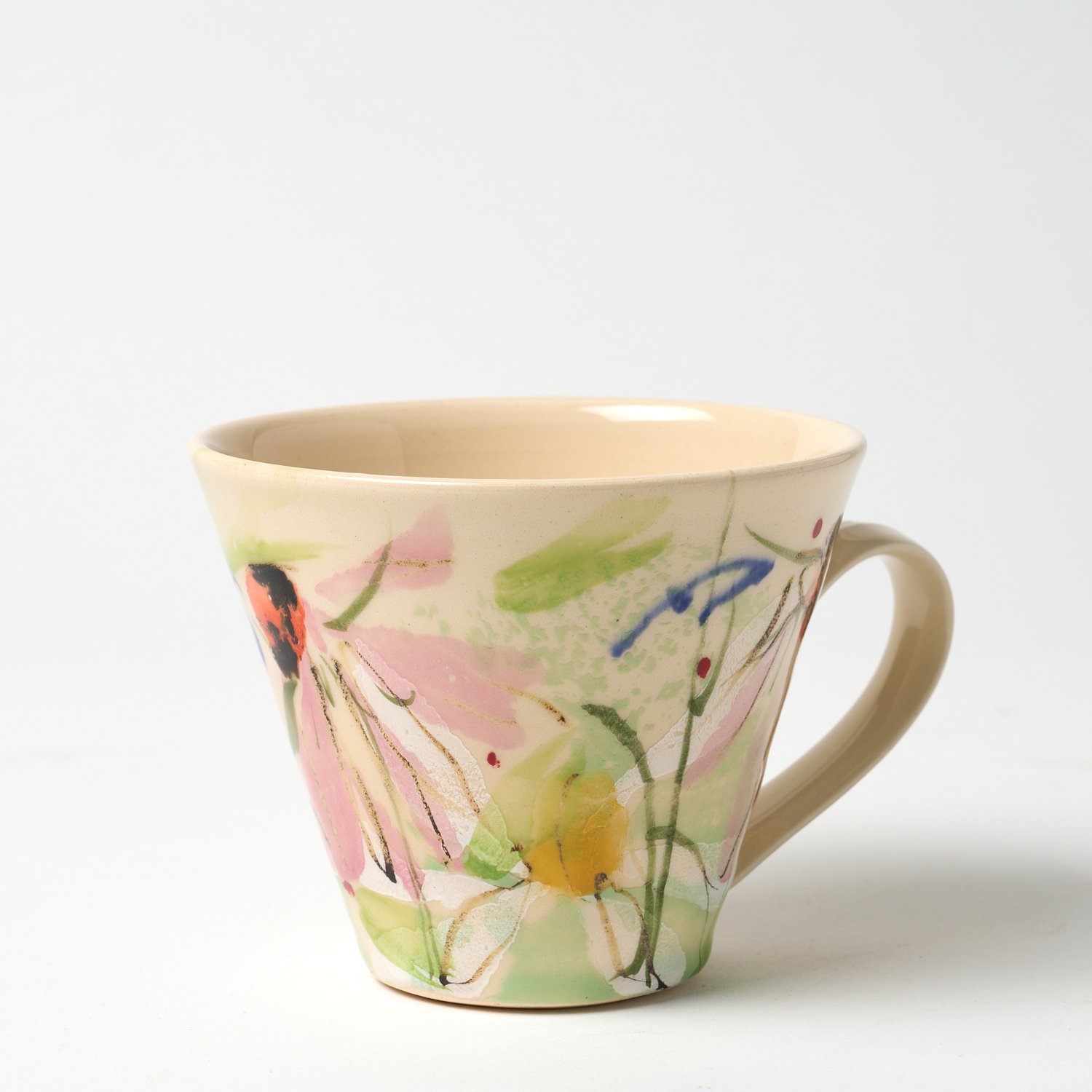 A photo of a hand thrown ceramic cup. It has a hand painted floral design on a light background glaze.