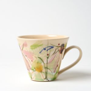 A photo of a hand thrown ceramic cup. It has a hand painted floral design on a light background glaze.