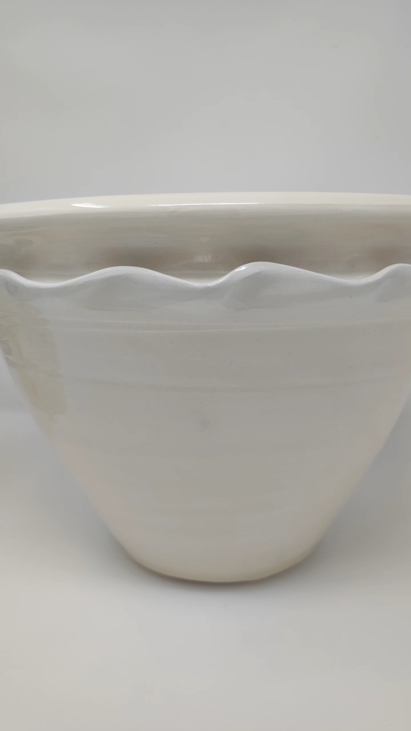 A photo of a hand thrown, white earthenware glazed cache pot.