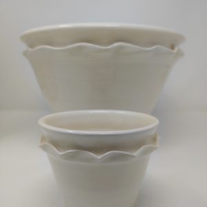 A photo of two hand thrown, white earthenware glazed cache pots. A smaller one sits in the front while at the back is a larger one.